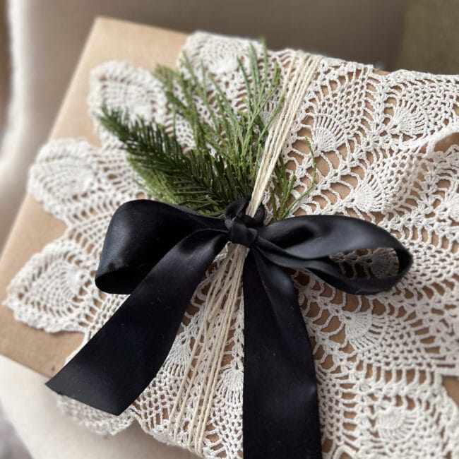 close up of brown package with vintage star doily, black ribbon and real greenery