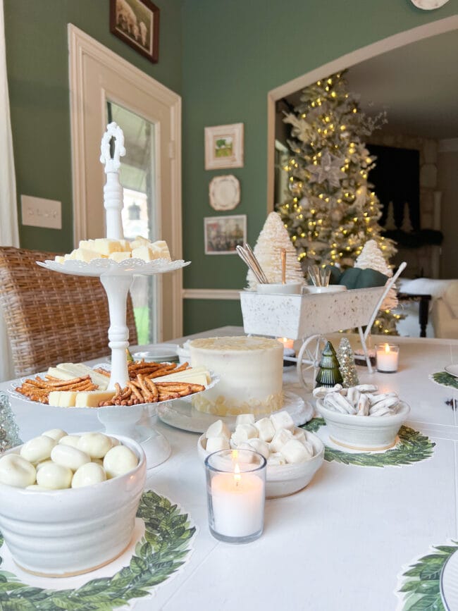 white cake and bowls of nuts and a 2 tiered dessert plate with cheese and pretzels