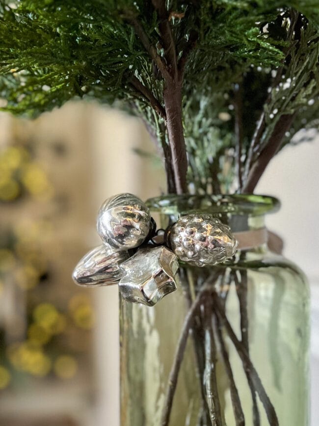 green vase with a cluster of small silver ornaments around neck 