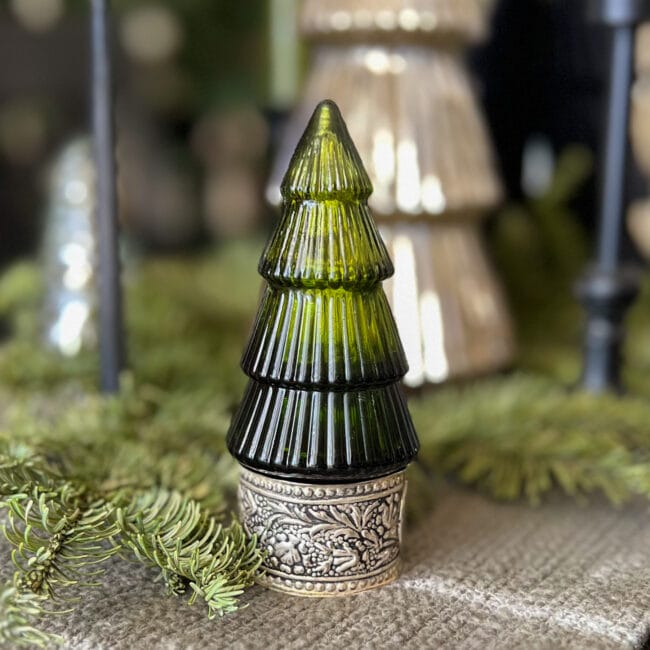 close up of a green glass tree on a silver napkin ring with real greenery around it