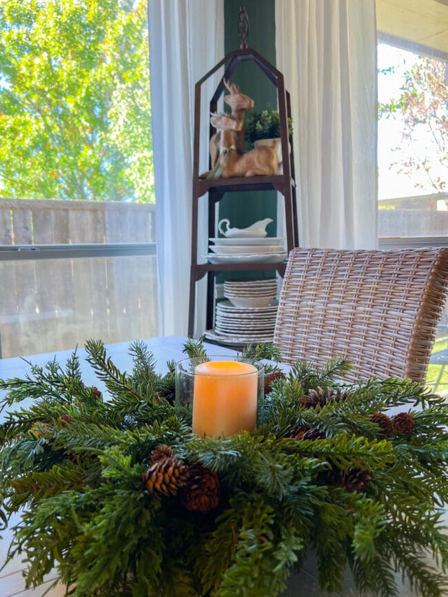 close up of greenery candle centerpiece with dishes on plate rack in front of windows