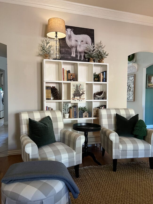 two checked chairs with a white cubby shelf behind them. The shelves have books, Christmas decor and a lamp on top