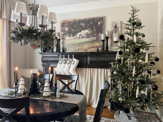 neutral dining room with black mantel with candles and hanging white stockings, Christmas tree in neutral colors and black table and chairs