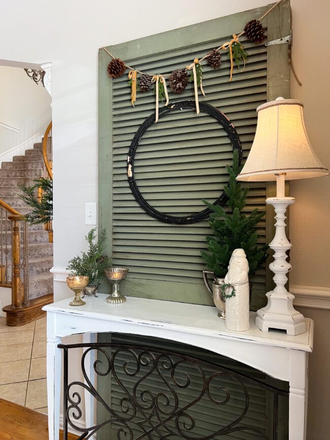 white console table with large green wooden screen behind it. Table has a lamp, small Christmas tree, white ceramic Santa and small antique candy dishes with tealights inside