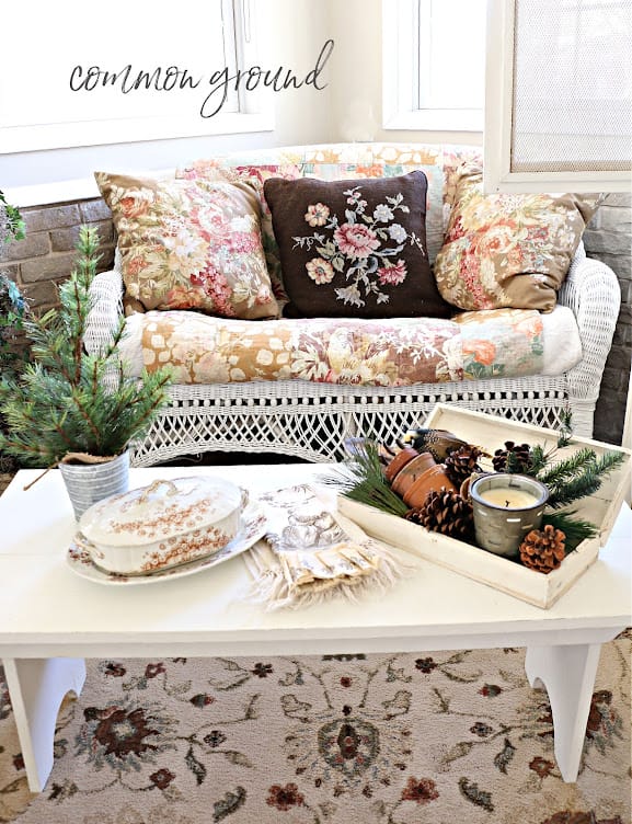 wicker love seat with warm floral pillows, a white coffee table with winter decor on it