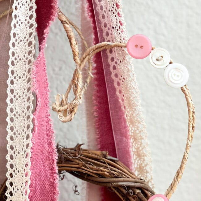 close up of rope heart with buttons and several pink ribbons and one lace ribbon