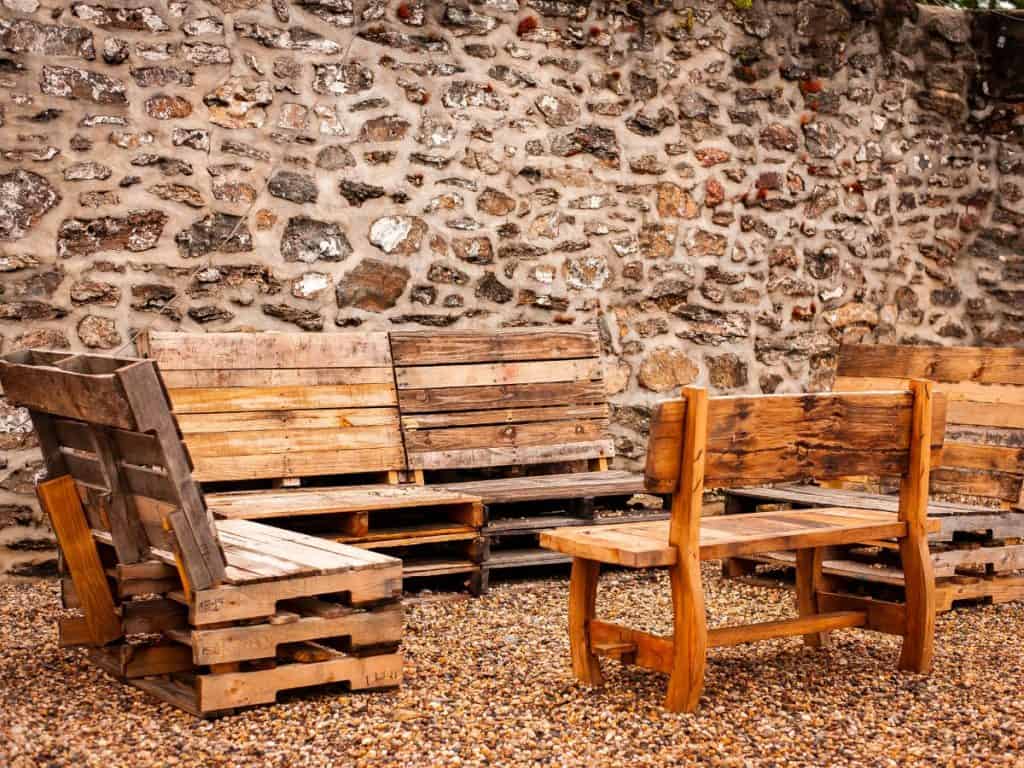 3 pallet chairs sitting with a gravel base and a stone wall behind them