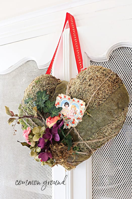 green moss heart with fresh flowers and a valentine card hanging on a hutch