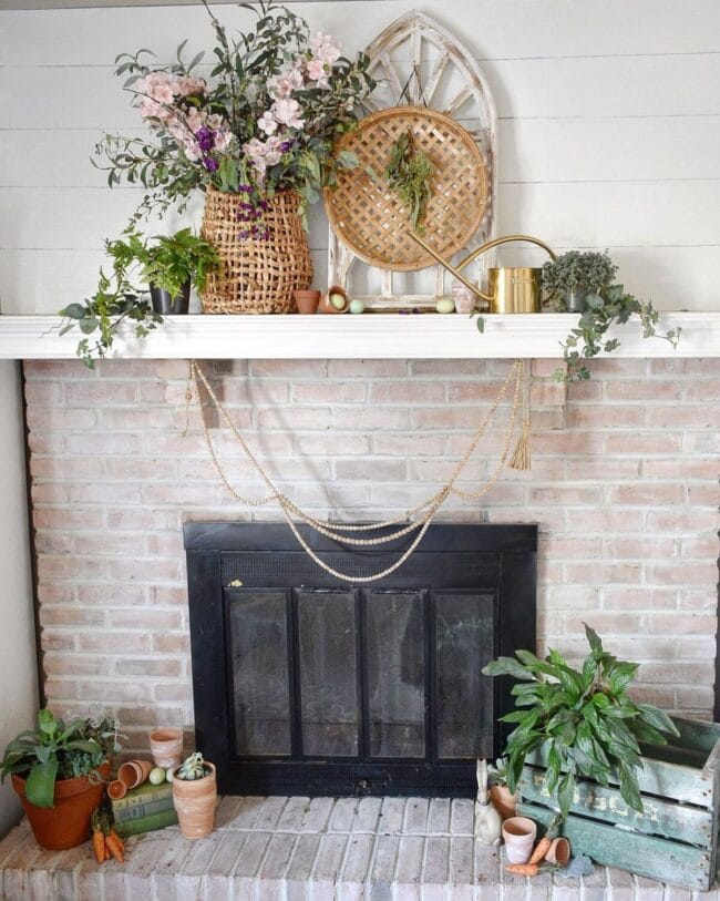 brick mantel with white mantel, hanging beads, basket of flowers and a round basket medallion hanging on a faux cathedral window