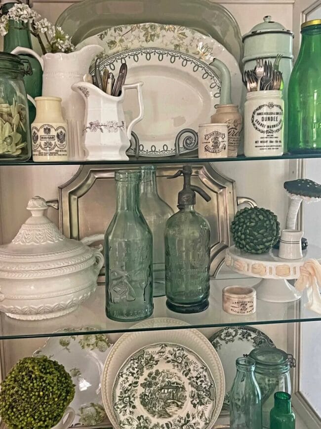 green bottles, plates, and other china on glass shelves