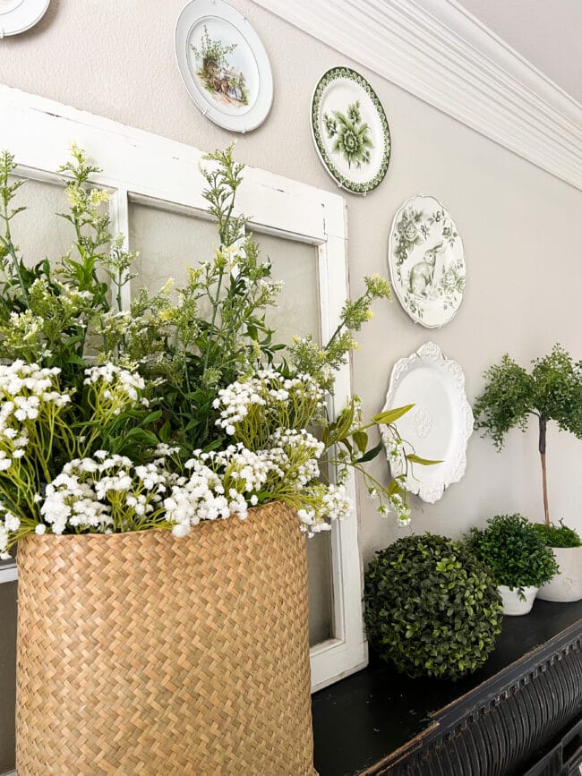 basket of flowers with green and white plates hung on wall around a white window