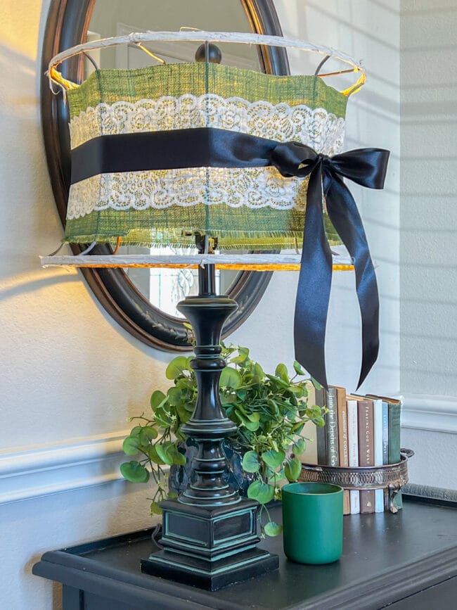 vintage lamp with green, white and black ribbon, a stack of books and green plant and candle