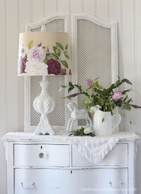 white lamp with a floral shade sitting on a white dresser with a plant