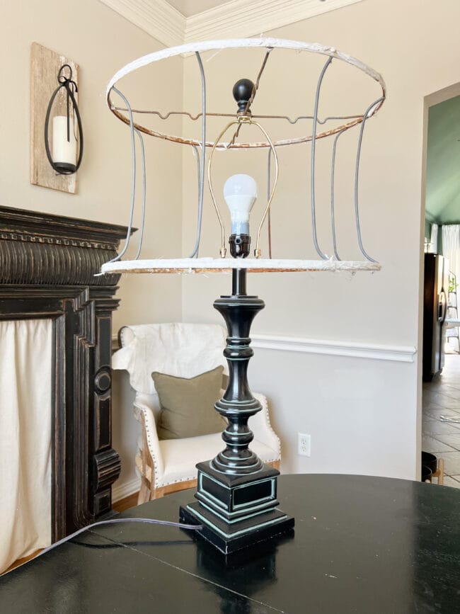 black lamp with empty lamp shade frame sitting on a black table with an armchair in the back ground