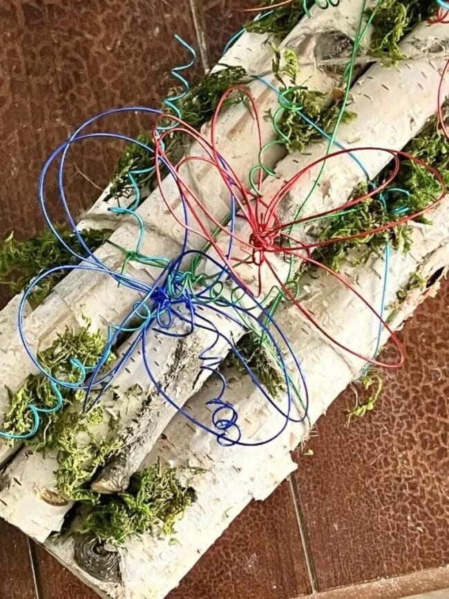 Birch logs stacked with moss and red, green and blue wire