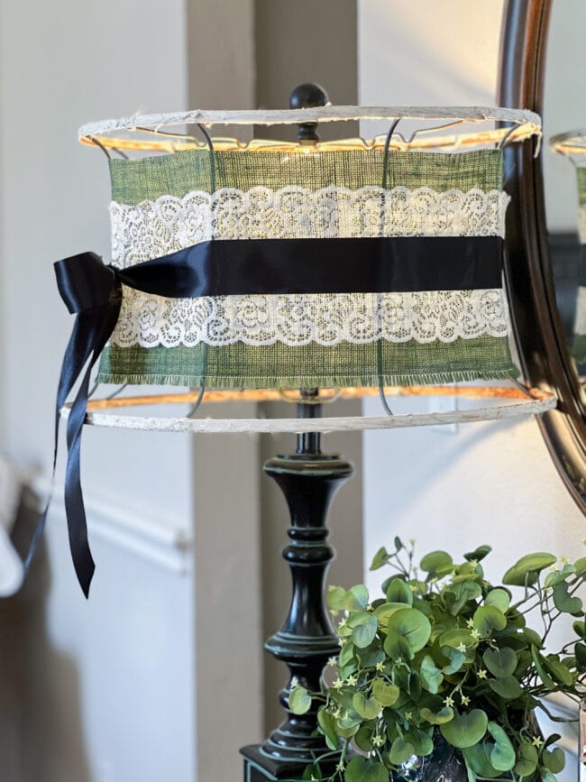 close up photo of the lampshade with green burlap, white lace and black ribbon tied in a bow.