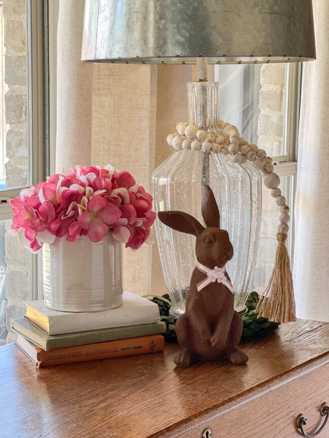 Table vignette with pink faux flower arrangement, glass lamp with beads and a brown rabbit