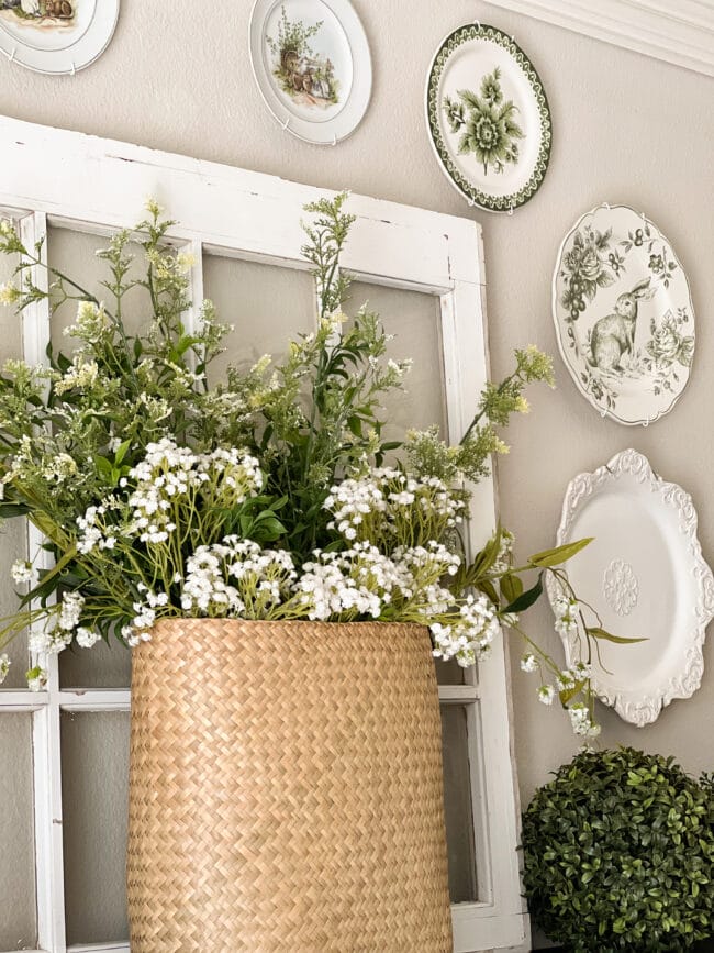 basket of green and white spring flowers sitting in front of a windowpane and bunny plates