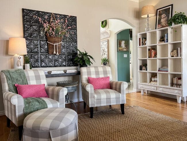 checked chairs with pink pillows in front of a sofa table with large metal wall art and plant