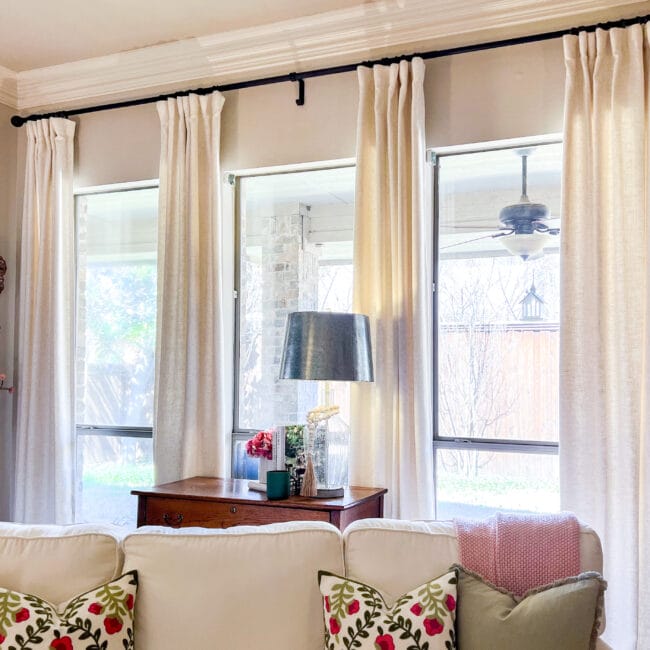 top of sofa with pink and green pillows and windows with beige curtains