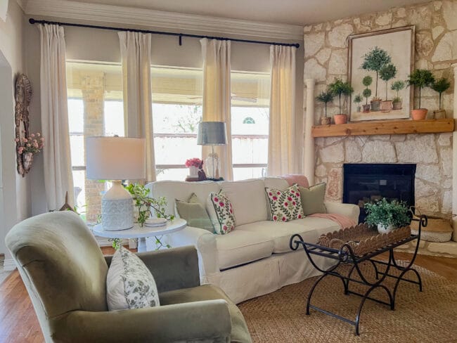 living room with windows, stone mantel, green chair and pink and green pillows on the white sofa