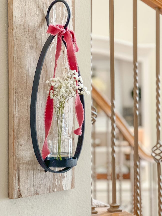 Wood and iron candle sconce with pink ribbon and a clear bottle with white flowers