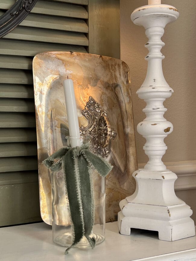 silver tray lid leaning against green door with a bottle and white candle and lamp