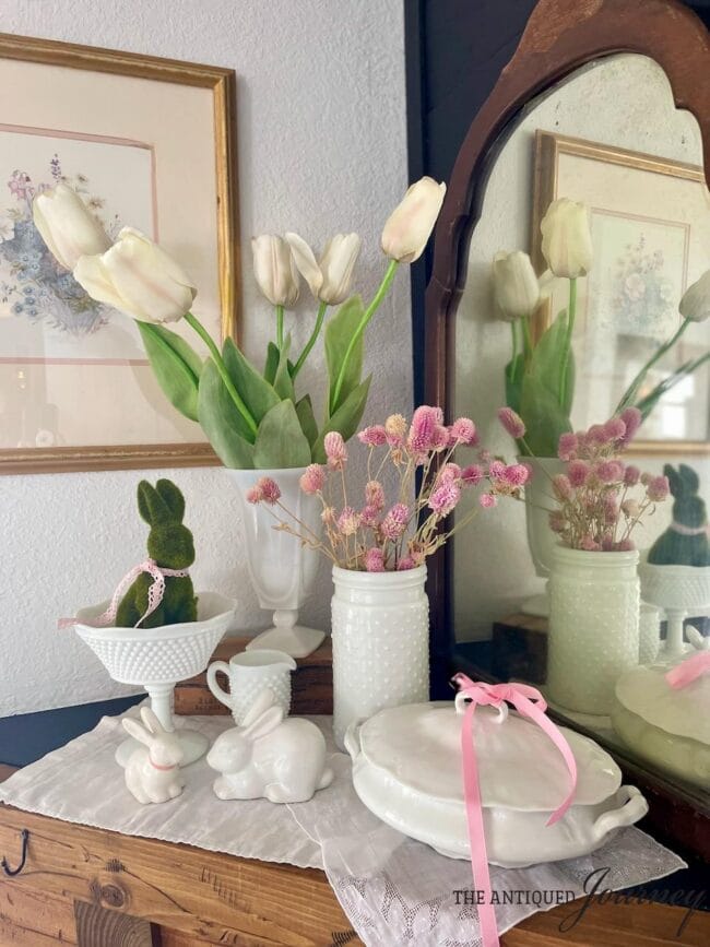 white milk galss with pink flowers, tulips and moss bunny displaced on a vintage dresser